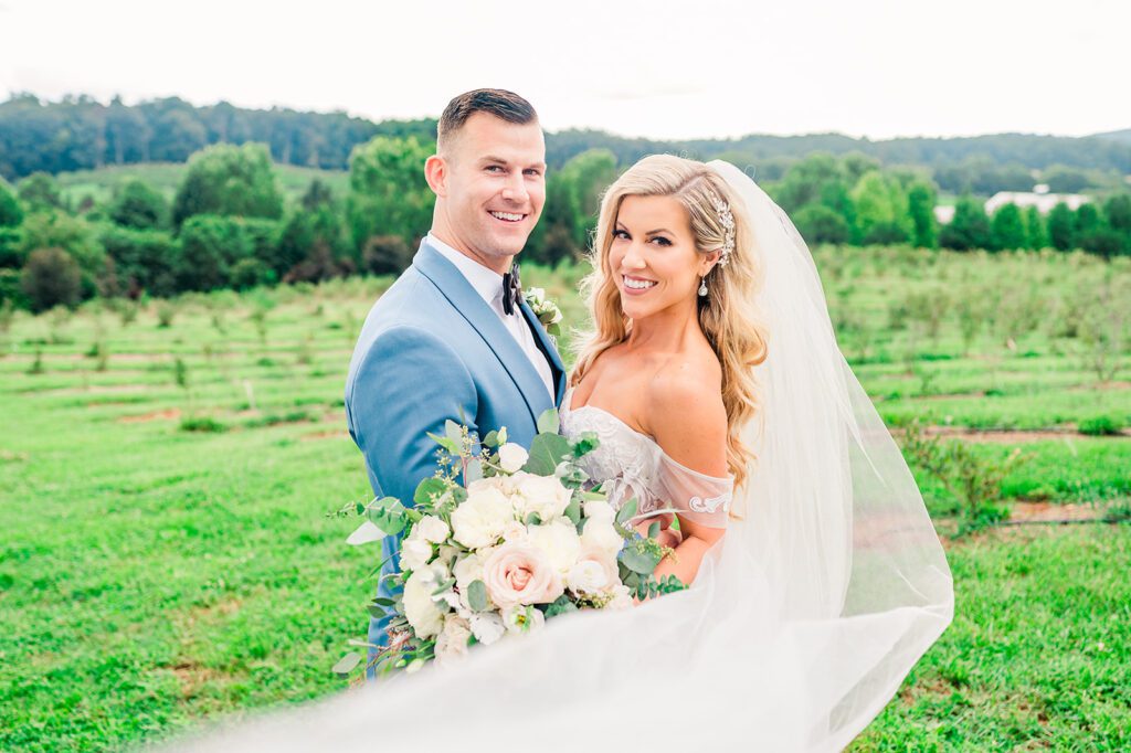 Bride and groom smiling in vineyard with veil blowing in the wind