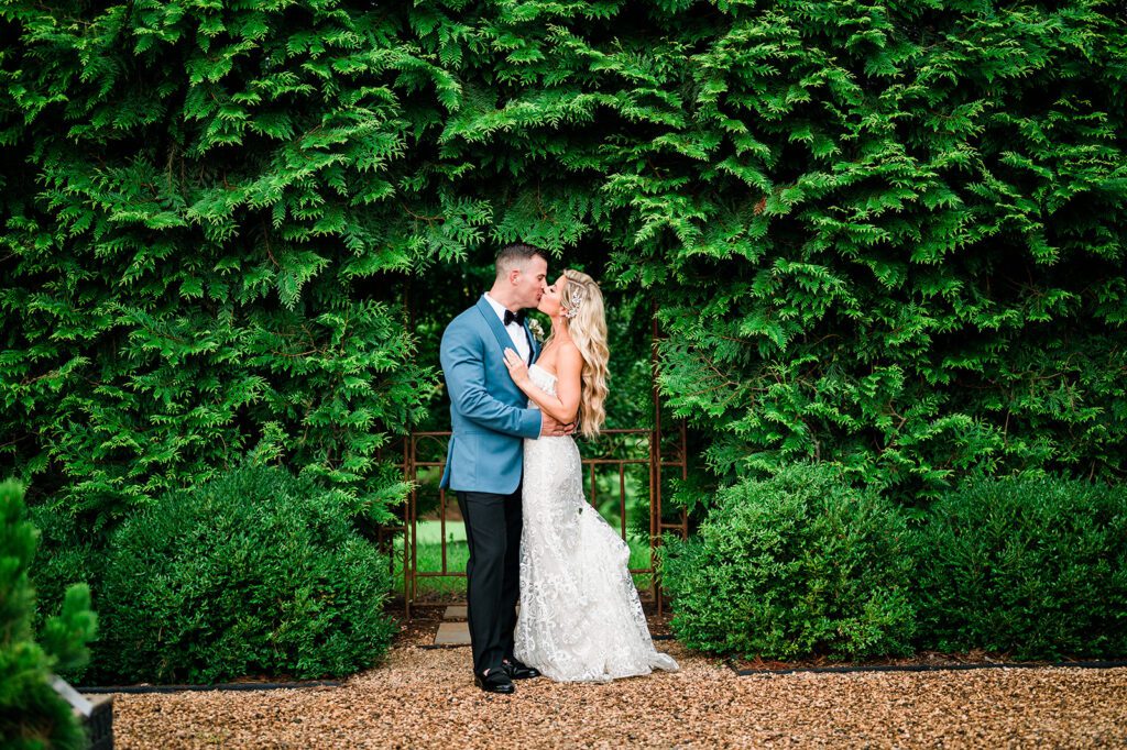 Bride and Green kissing in from of greenery outside